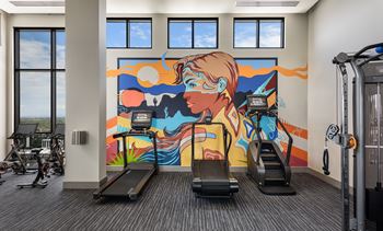 A gym with treadmills and a colorful mural on the wall.